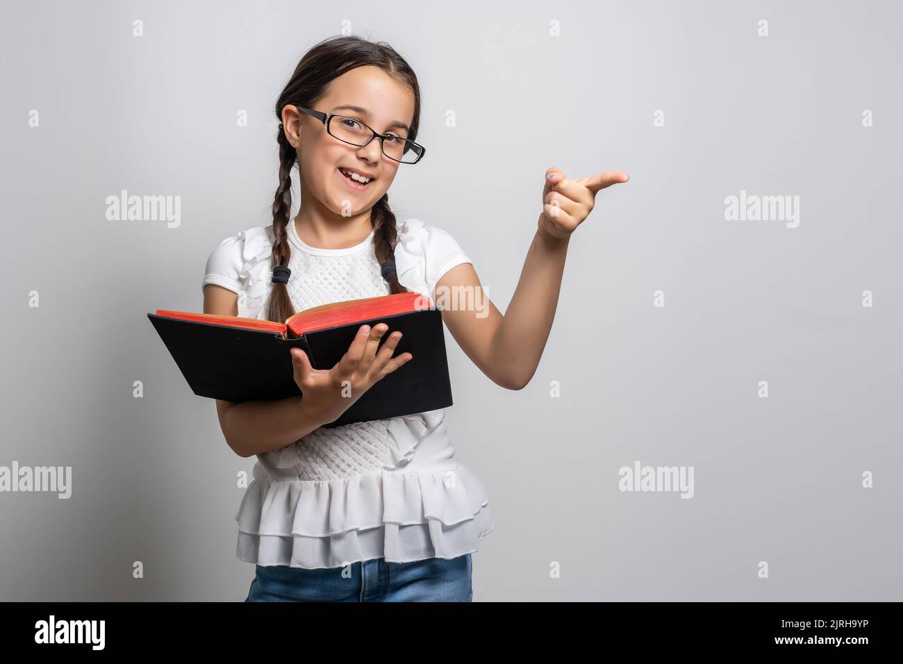 Lovely little girl standing and holding book over white background ...
