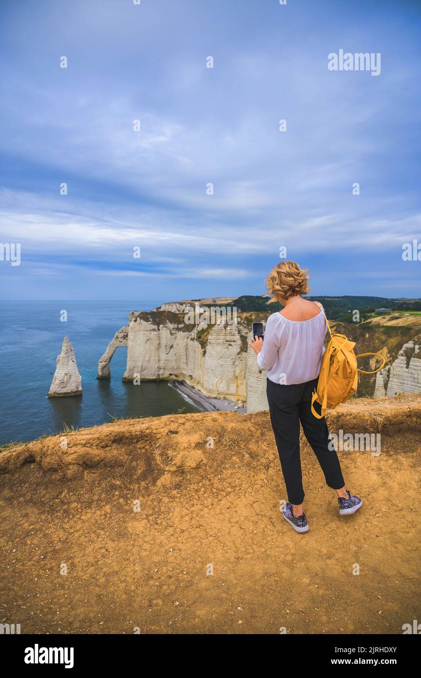 Travel concept - tourist takes picture of Etretat on the white cliffs at the viewpoint, blue skies and cliff views, Etretat, France, Normandy  Stock Photo