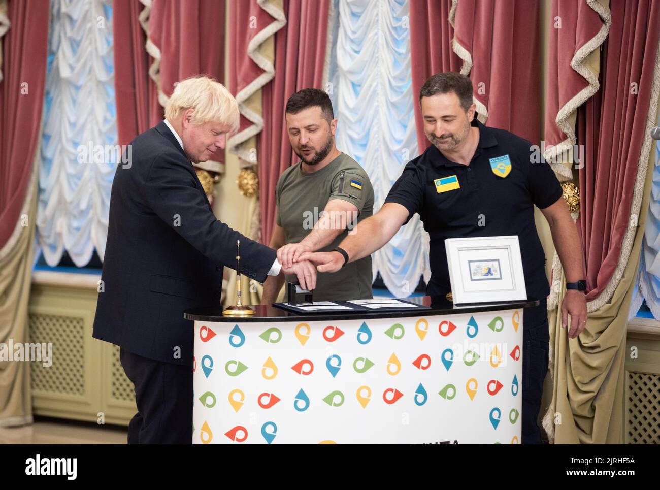Lviv, Ukraine. 24th Aug, 2022. British Prime Minister Boris Johnson, left, Ukrainian President Volodymyr Zelenskyy, center, and Ukrposhta Director Ihor Smilianskyi, right, cancel the first set of the newly issued postage stamp marking the last six month of the Russian Invasion during a ceremony at the Mariinsky Palace, August 24, 2022 in Kyiv Ukraine. The stamp called “Free, Unbreakable, Unbeatable”, was released for the 31st anniversary of Ukraine independence. Credit: Sarsenov Daniiar/Ukraine Presidency/Alamy Live News Stock Photo