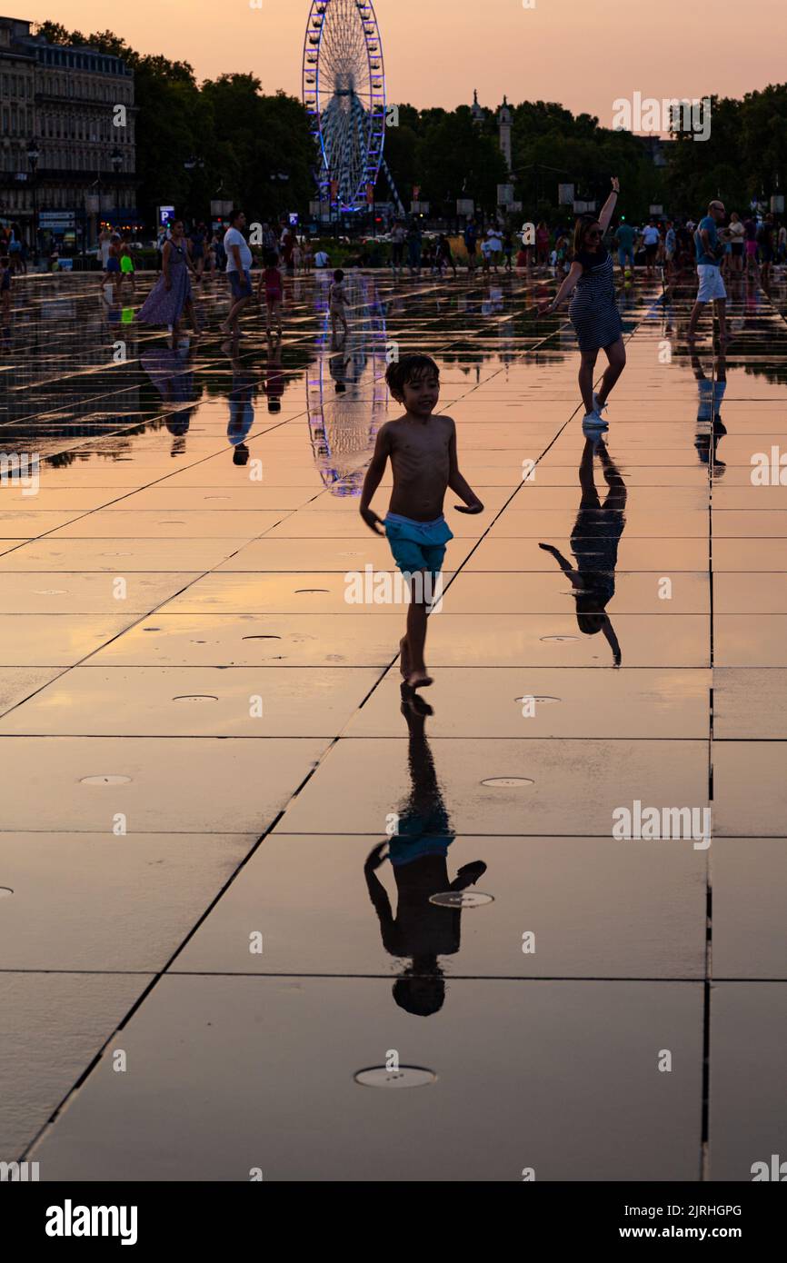 Bordeaux, France - July, 17: Child at sunset having fun walking in the water mirror fountain at Place de la Bourse in Bordeaux, Aquitaine on July 17, Stock Photo