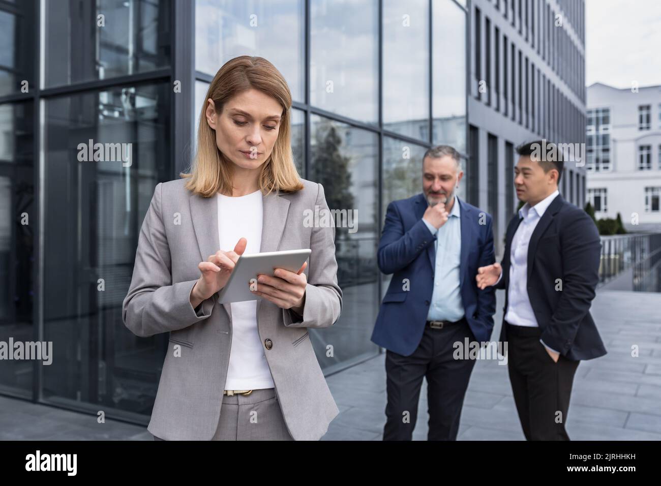 Harassment at work, group of business people outside office building, men discussing behind woman boss's back, gossiping and stalking Stock Photo