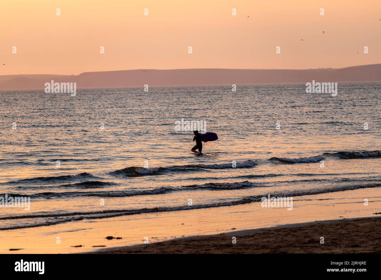 Learning to surf in Broad Haven beach at sunset, Broad Haven, seaside resort  St Bride's Bay, Pembrokeshire, Wales, UK Stock Photo