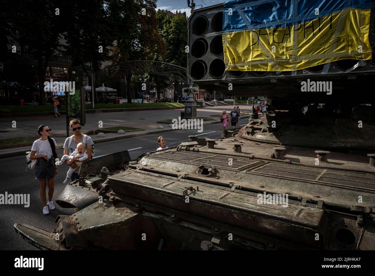 Kyiv, Ukraine. 22nd Aug, 2022. A family observes the wreckage of a Russian Multi-Rocket Launch System (MLRS) vehicle with a Ukrainian national flag in Kyiv. As dedicated to the upcoming Independence Day of Ukraine, and nearly 6 months after the full-scale invasion of Ukraine on February 24, the country's capital Kyiv holds an exhibition on the main street of Khreschaytk Street showing multiple destroyed military equipment, tanks and weapons from The Armed Forces of The Russian Federation (AFRF).As the Russian full invasion of Ukraine started on February 24, the war that has killed numerous c Stock Photo