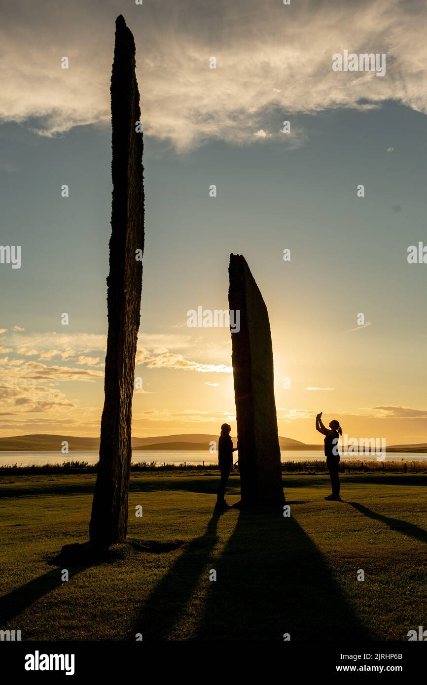 Orkney, UK. 24th Aug, 2022. Two women are dwarfed as they stand next to a stone in the Standing Stones of Stenness, Orkney, as the sun sets. The 5,000 year old massive stones are part of the Heart of Neolithic Orkney World Heritage Site. Credit: Peter Lopeman/Alamy Live News Stock Photo