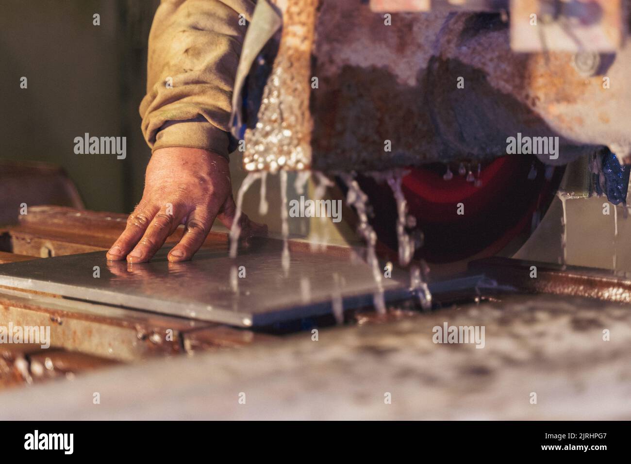 A closeup of a male hand cutting a tile with a machine Stock Photo