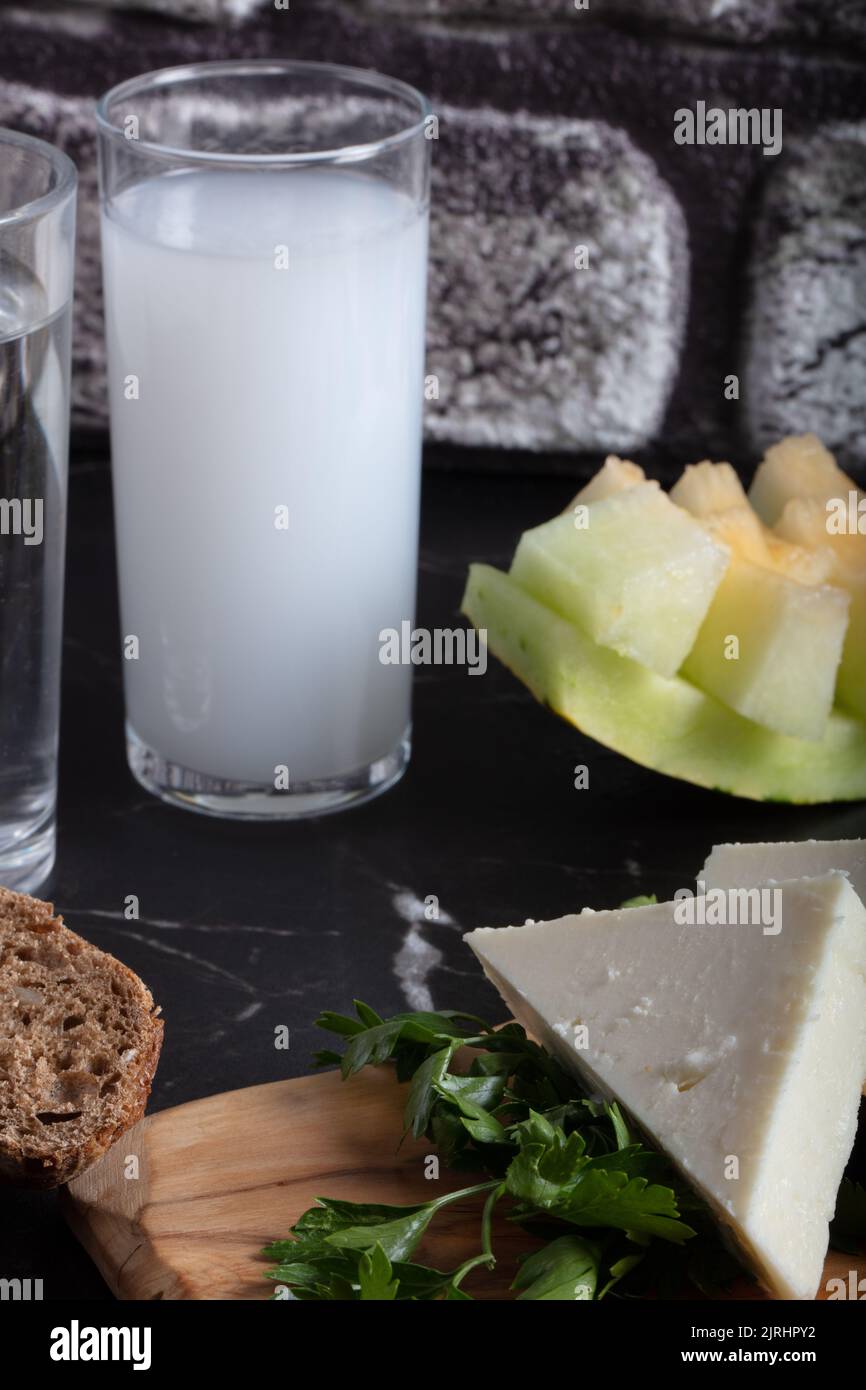 Turkish Raki with water on table with sliced melon and appetizer, traditional Turkish alcohol known as Raki, chill with friends at restaurant, dinner Stock Photo