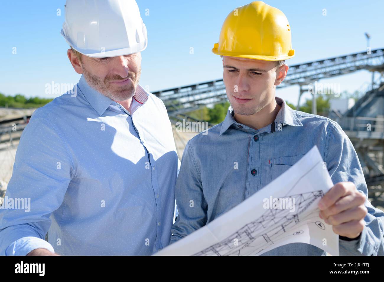 group of engineers wearing hardhats discussing over plans Stock Photo