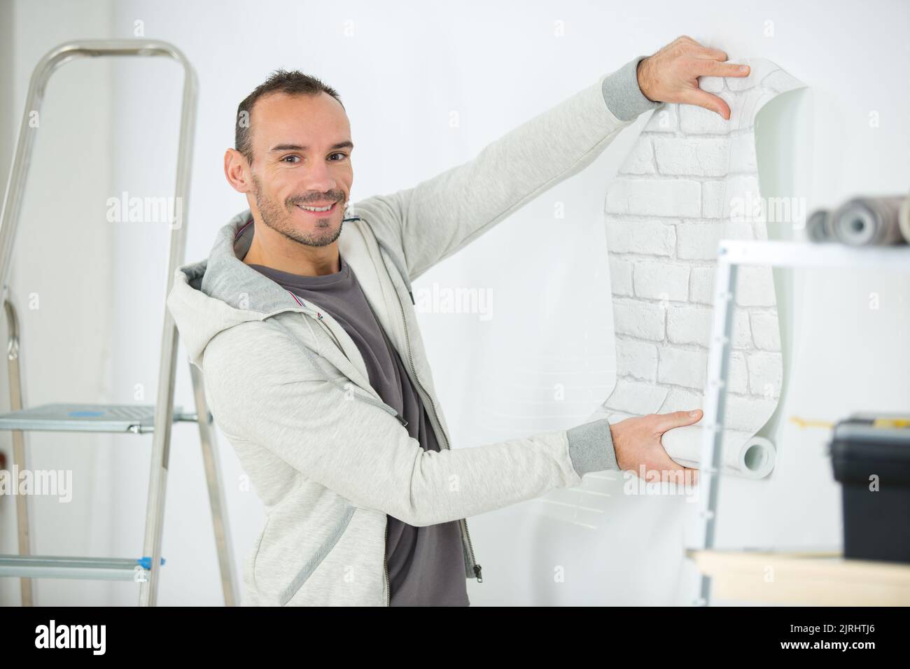 handyman putting up wallpaper on the white walls Stock Photo - Alamy