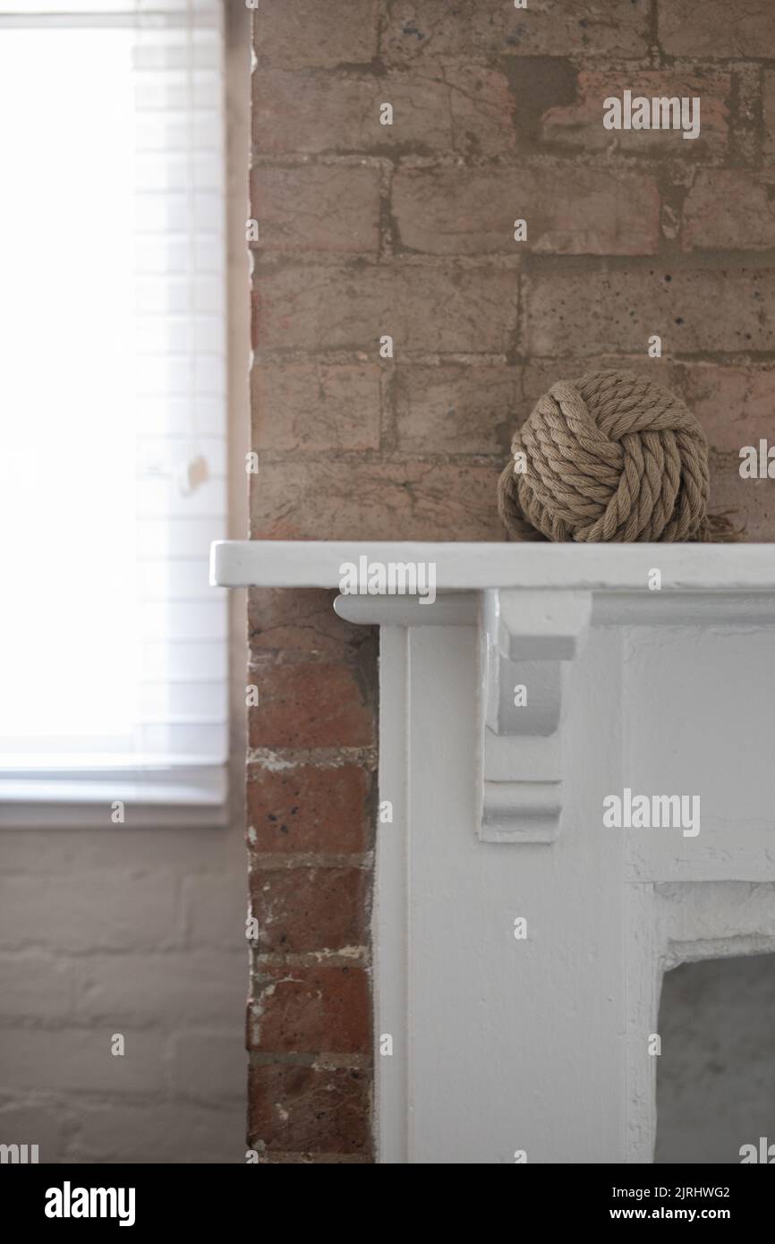 A vertical closeup of a modern interior with a beige knitting ball on a white fireplace in front of a brick wall Stock Photo