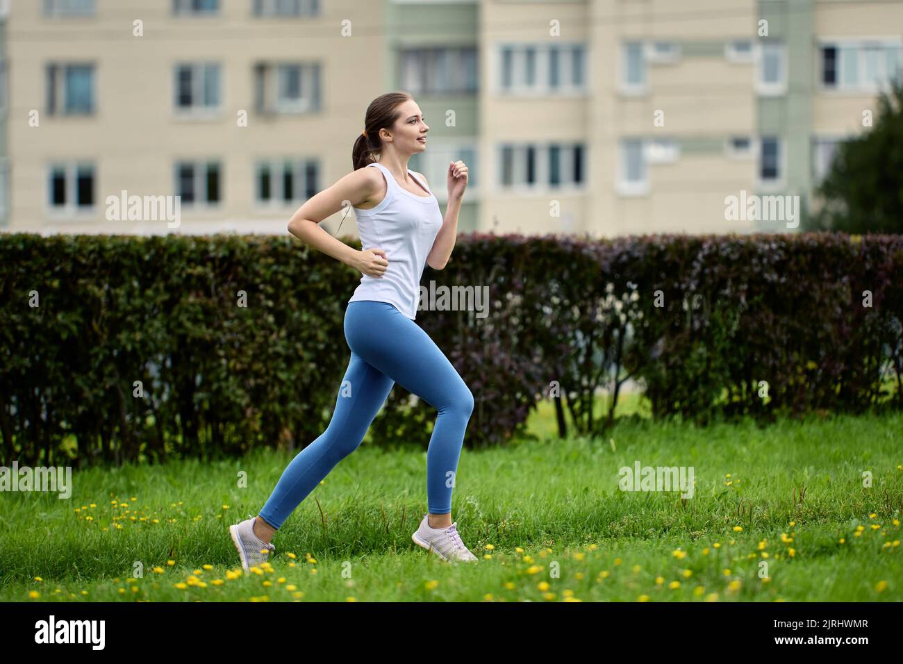 29 year old woman runs in park area of residential area near of residential multi apartment high rise building. Stock Photo