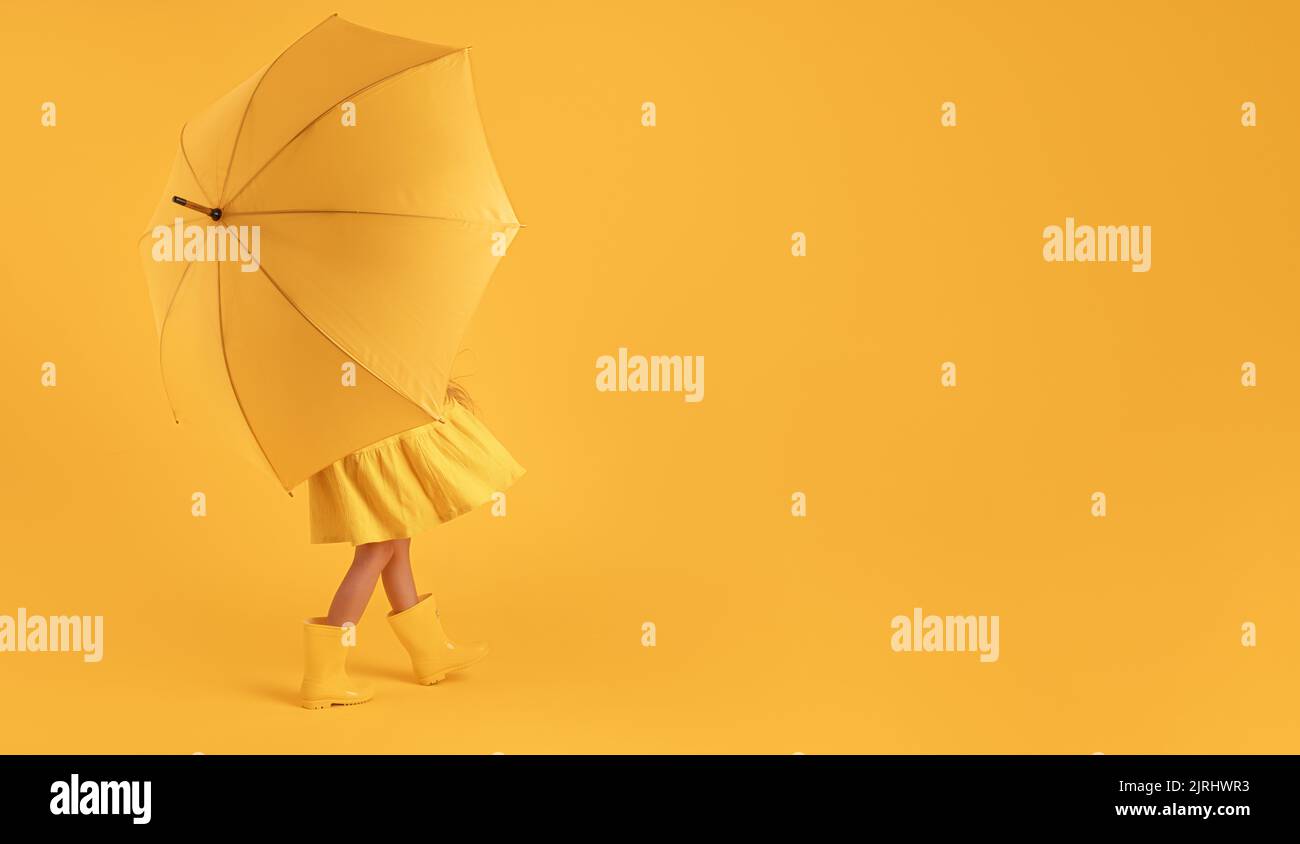 Girl with rubber boots for rain and umbrella over yellow background Stock Photo