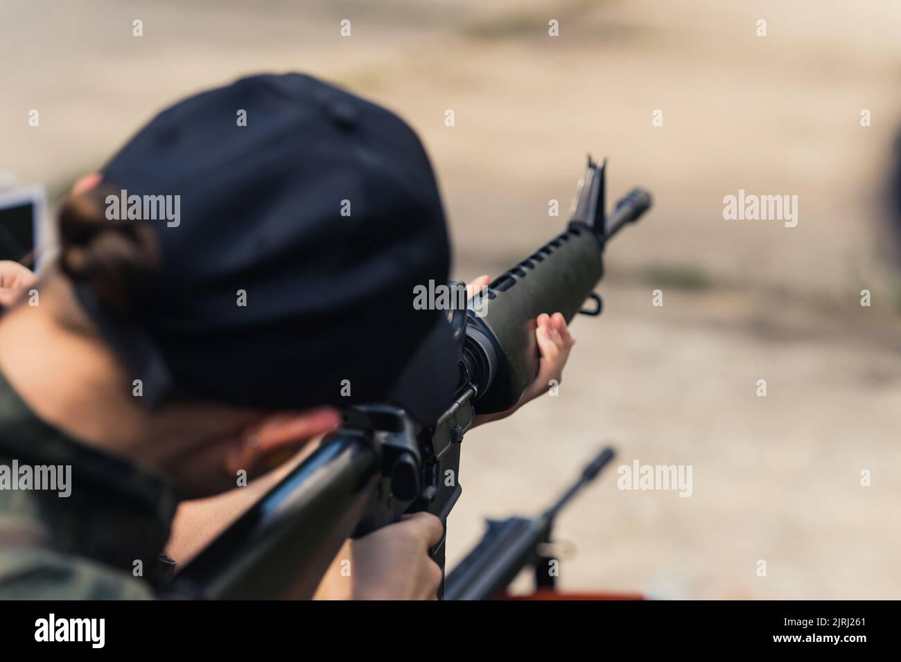 08.07.2022 Warsaw, Poland Unrecognizable caucasian person in a black baseball hat using brand-new M16 rifle. Blurred background. Outdoor shooting range. High quality photo Stock Photo