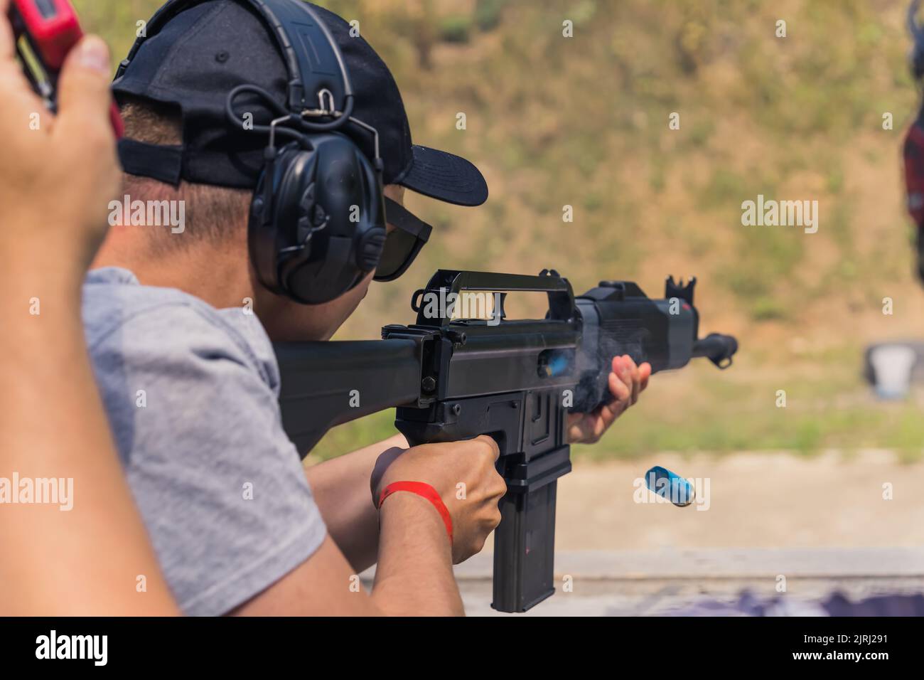 08.07.2022 Warsaw, Poland Unrecognizable caucasian man in gray t-shirt, black baseball cap, and protective headphones aiming with a black shotgun. Shooting competition. . High quality photo Stock Photo