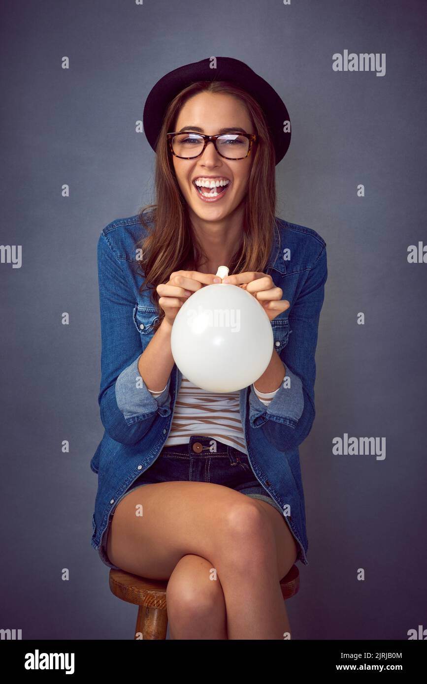Live a little, laugh a lot. a fun-loving young woman blowing up a balloon in studio. Stock Photo