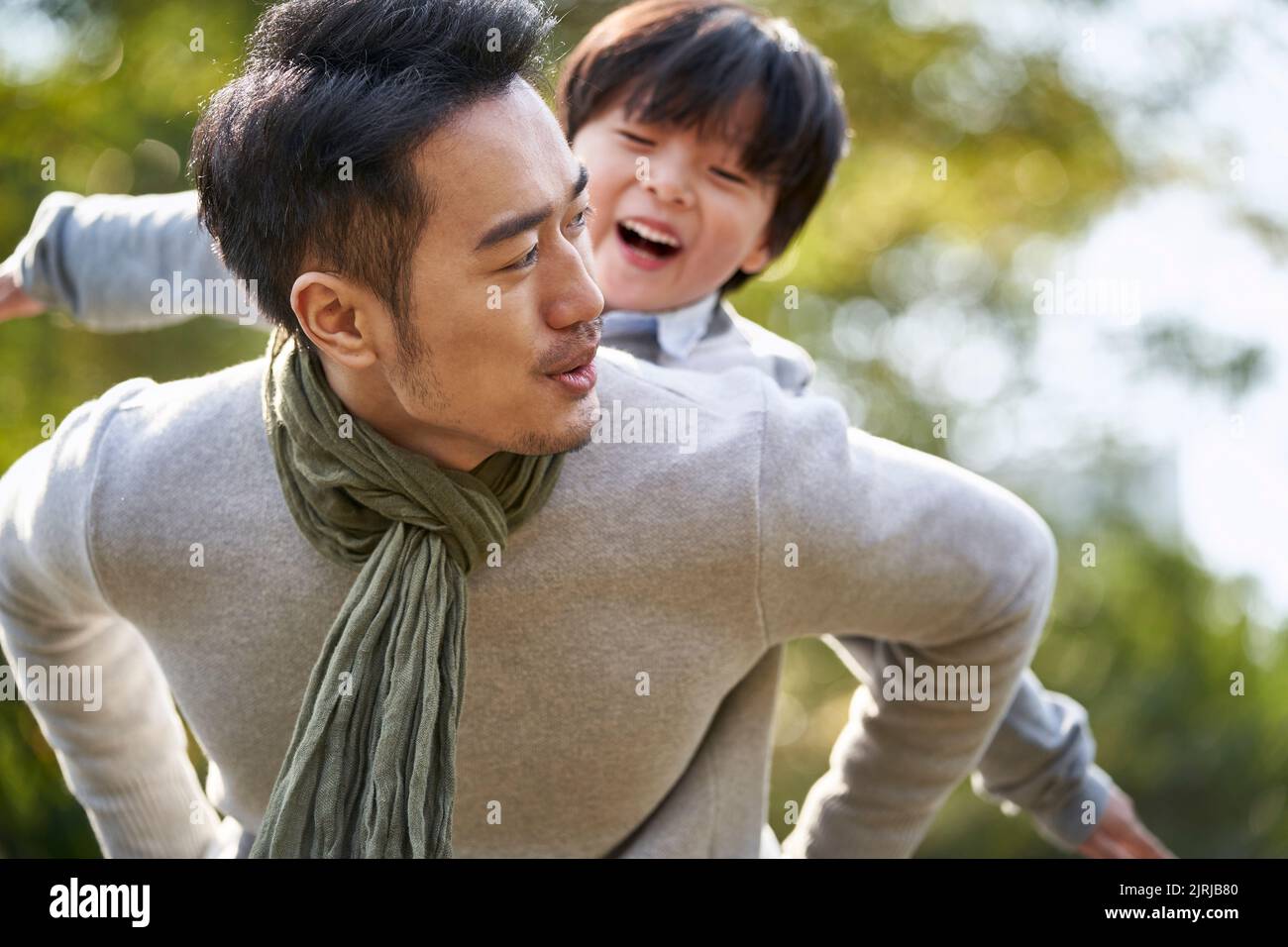 young asian father carrying son on back having fun enjoying nature outdoors in park Stock Photo