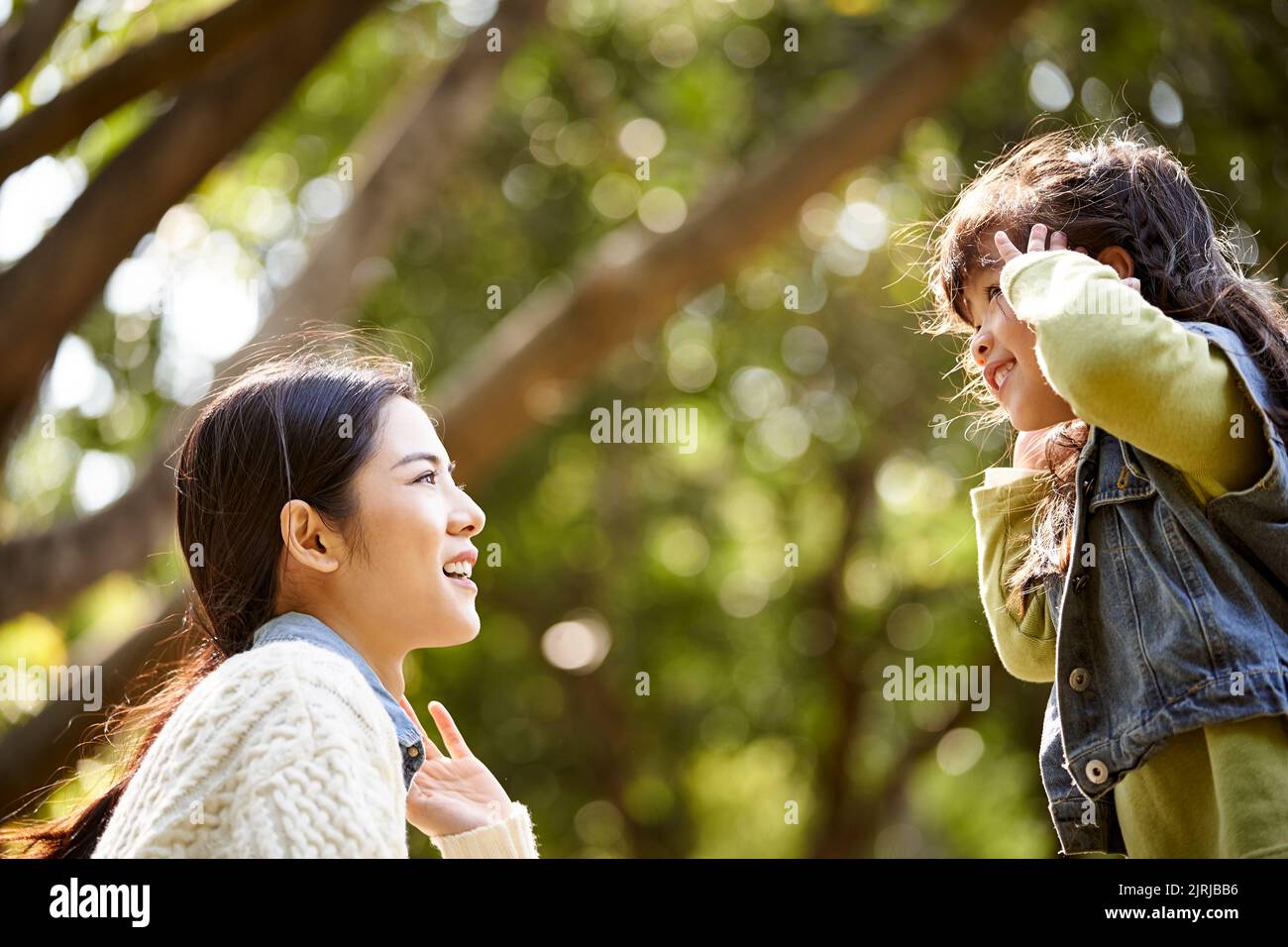 young asian mother sitting on grass in park having a pleasant conversation with cute daughter Stock Photo