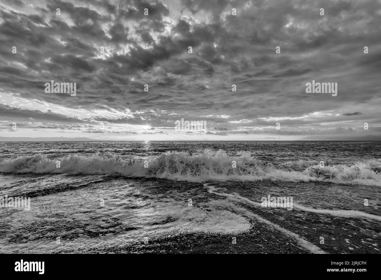 An Ocean Wave Is Breaking Against A Colorful Sunset Sky Black And White Stock Photo