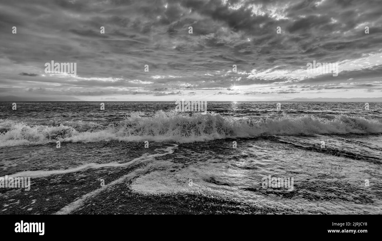 An Ocean Wave Is Breaking With Clouds Overhead Black And White Stock Photo