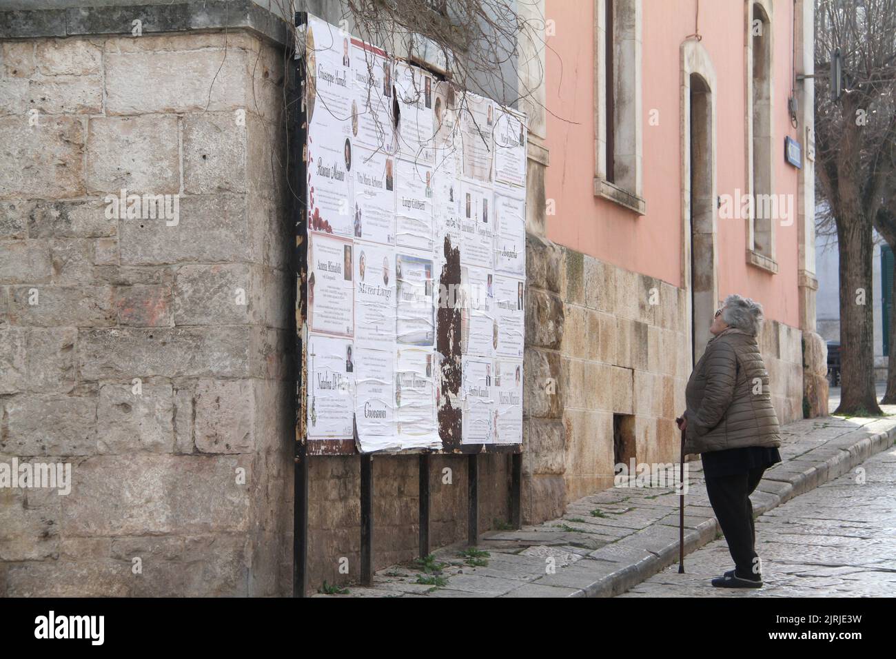 Elderly woman reading the obituaries posted on a city street in Italy
