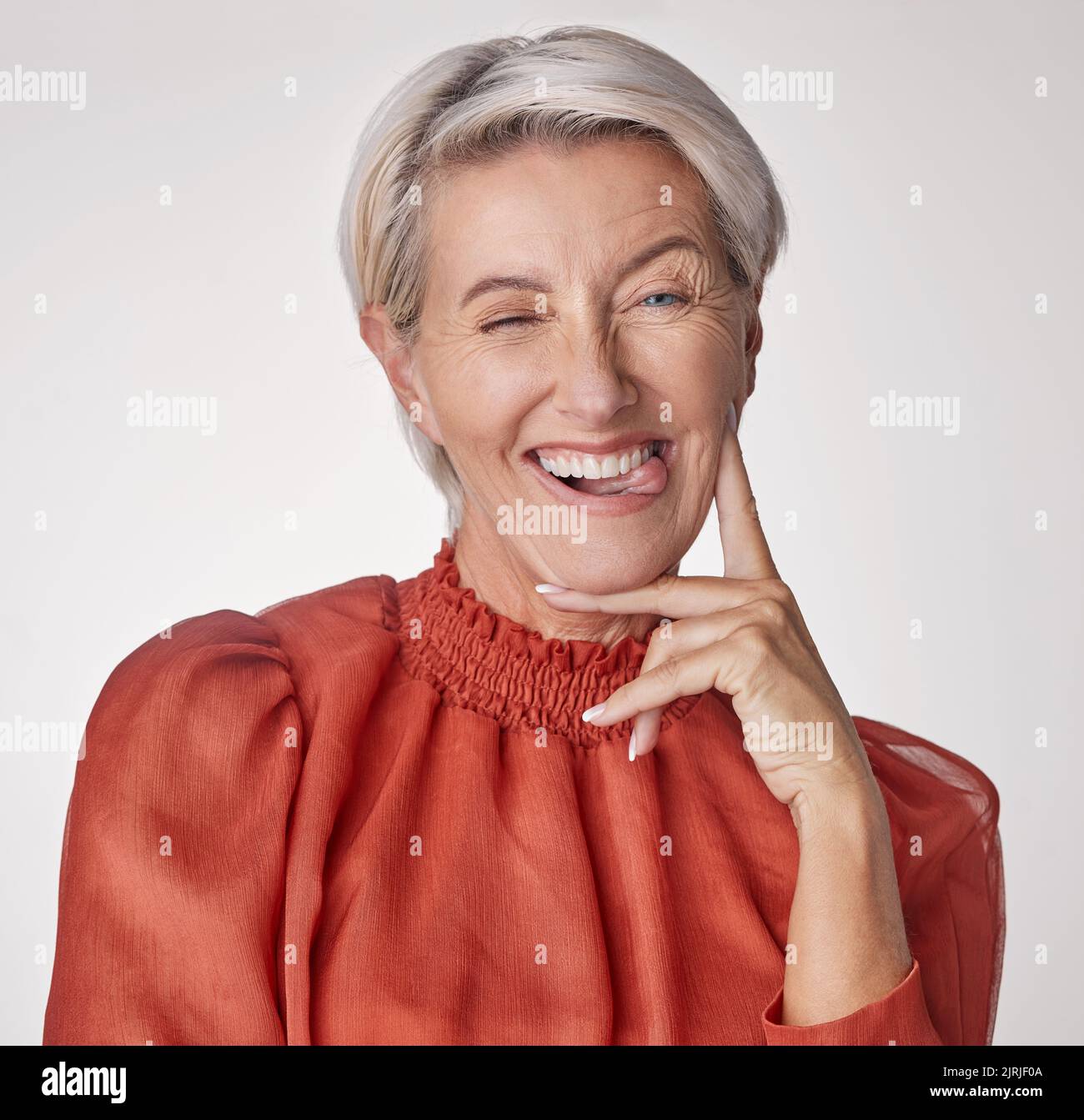 Comic portrait, quirky model or playful mature woman on gray studio background with funny facial expression, tongue or happy wink face. Silly, classy Stock Photo