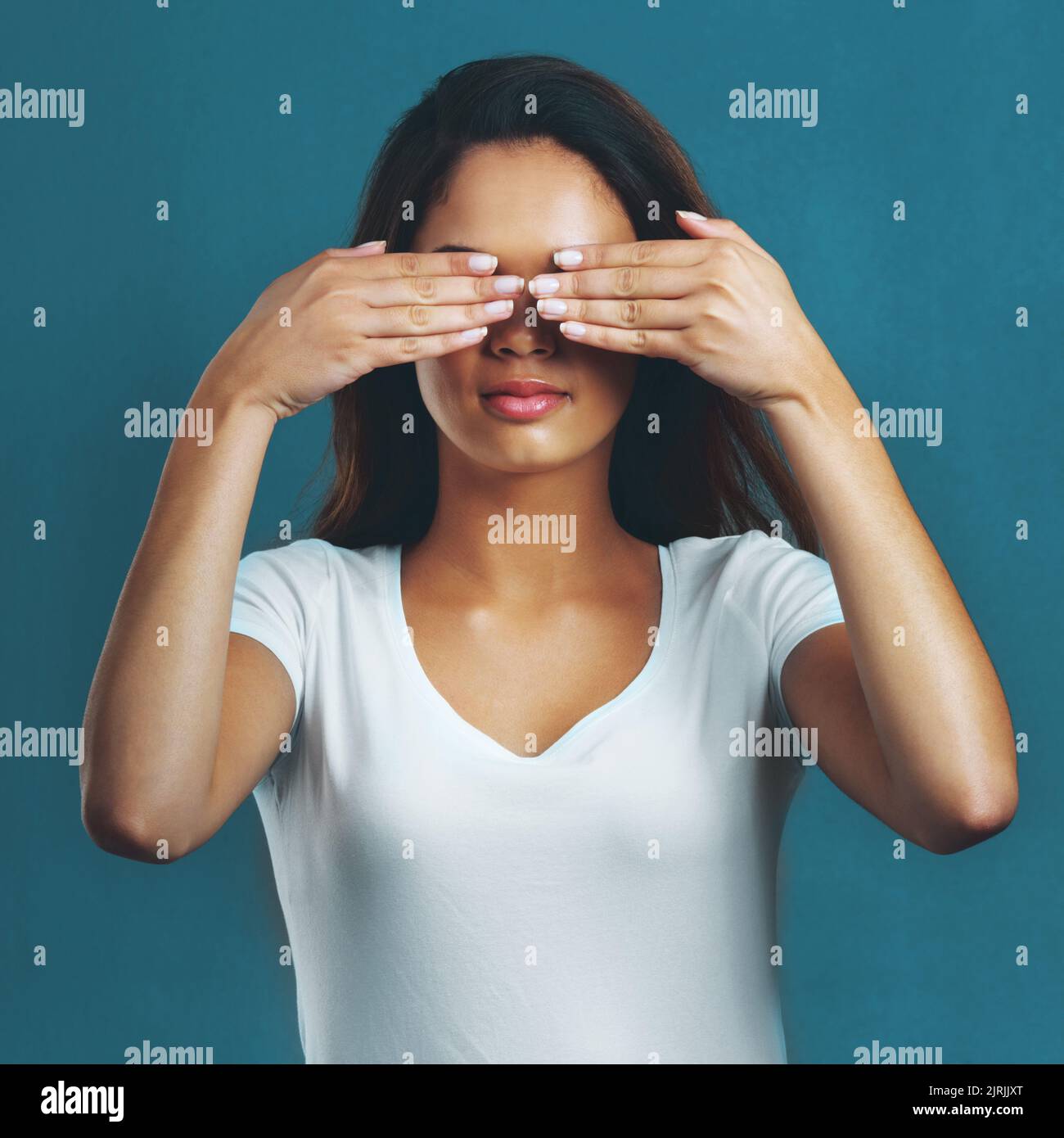 I didnt see anything. Studio shot of an attractive young woman covering her eyes against a blue background. Stock Photo
