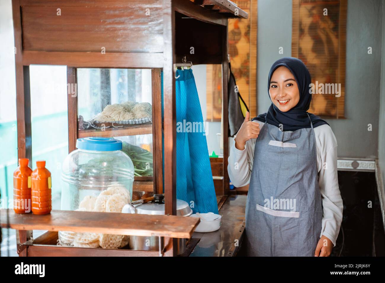 hijab woman wearing apron smiling while standing with thumbs up Stock