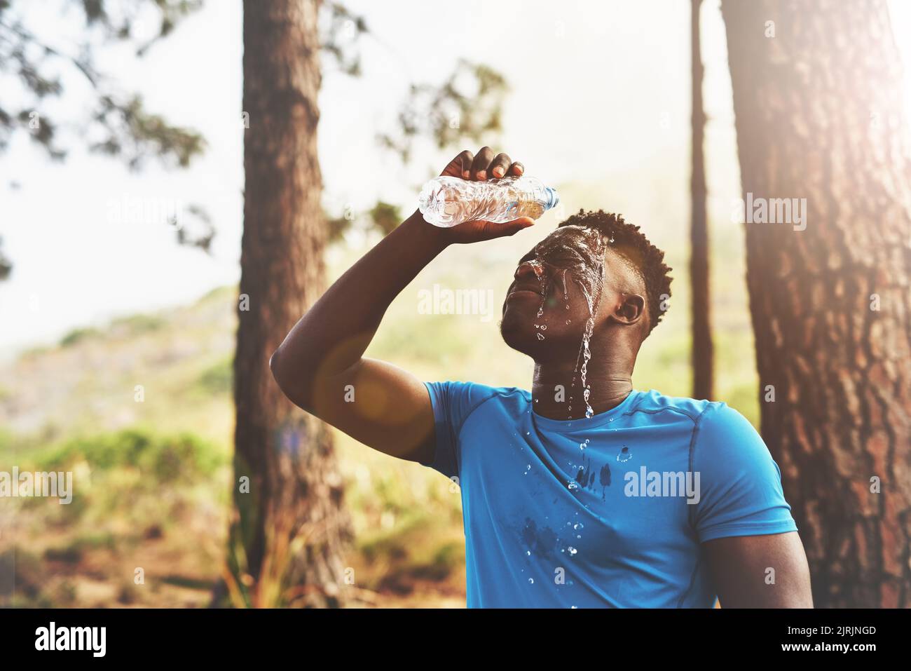 Cooling down after an intense workout. a sporty young man pouring water over his face while out for a run in the forest. Stock Photo