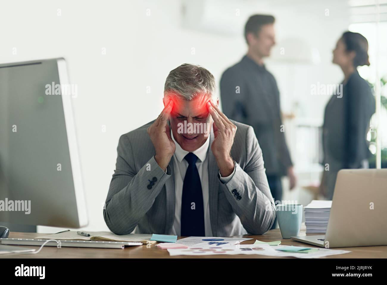 How do I stop this hammering in my head. a businessman with a headache holding his head while sitting at his desk. Stock Photo