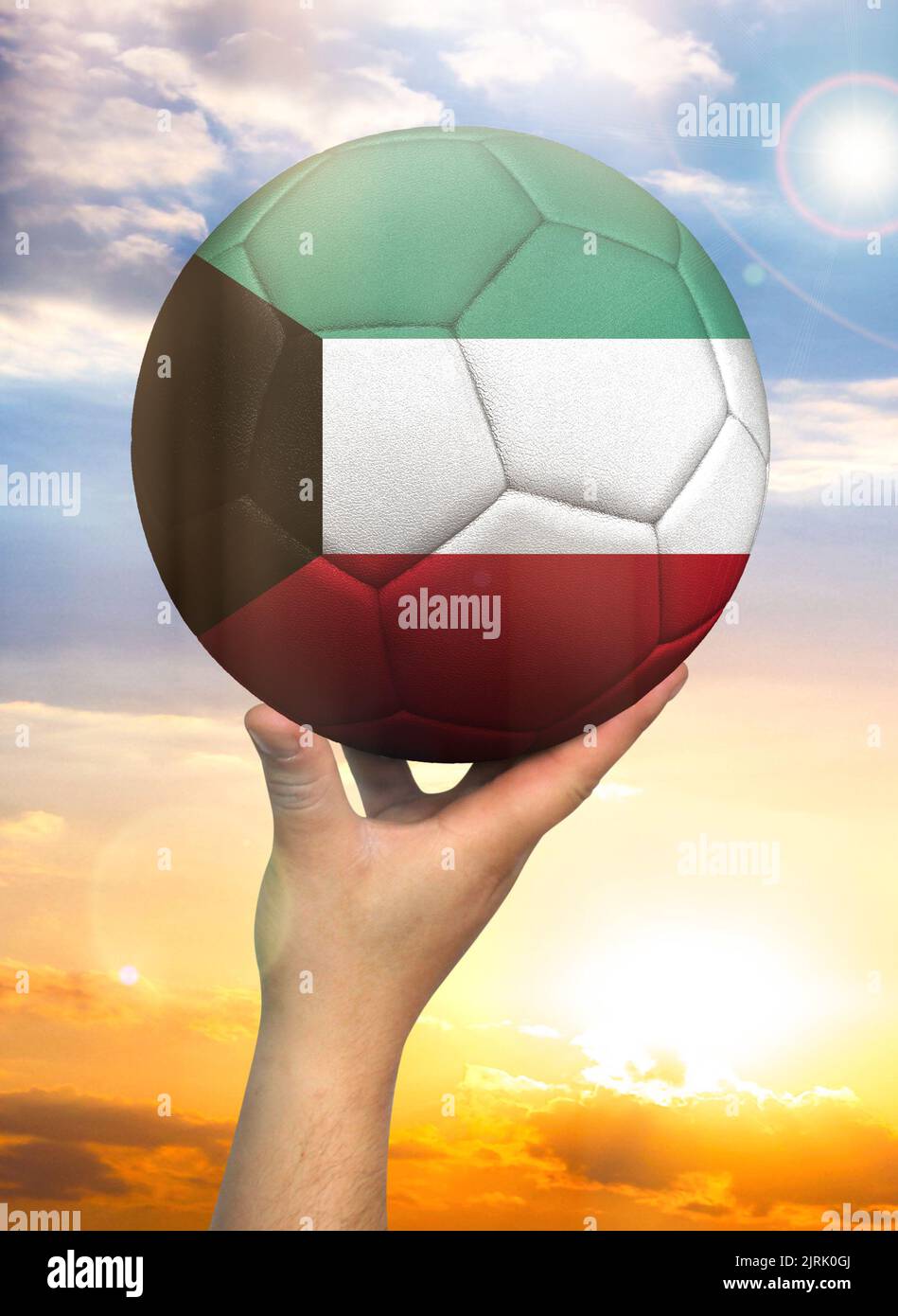 Soccer ball in hand with a depiction of the flag of Kuwait against a colorful sky Stock Photo