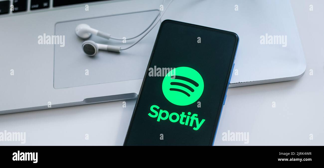 Close up view of a smartphone with Spotify logo on display. Laptop and ...