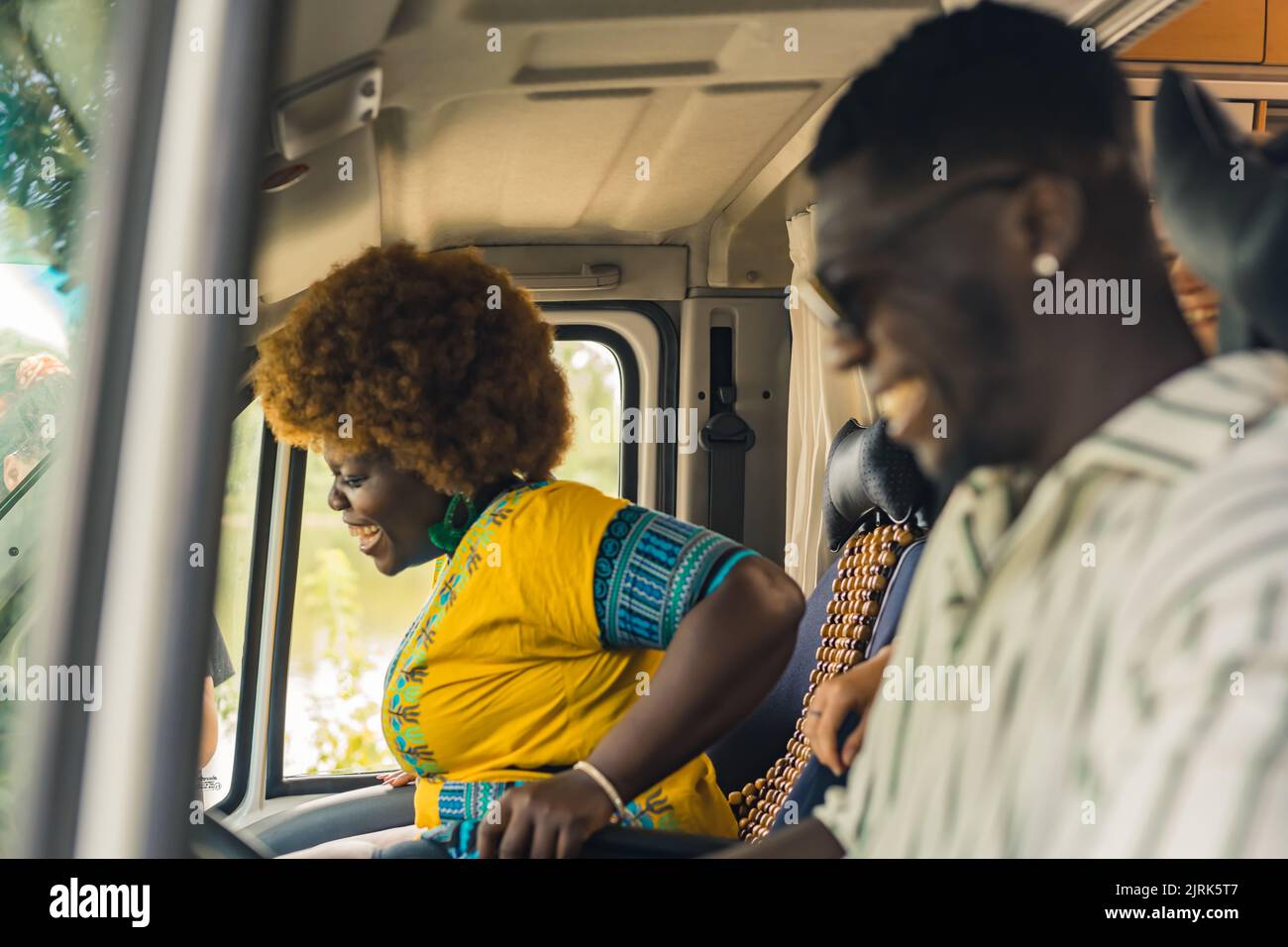 Ethnic dark-skinned straight couple having a summer road trip in a camping van, driving, talking and laughing heartily inside their vehicle. High quality photo Stock Photo