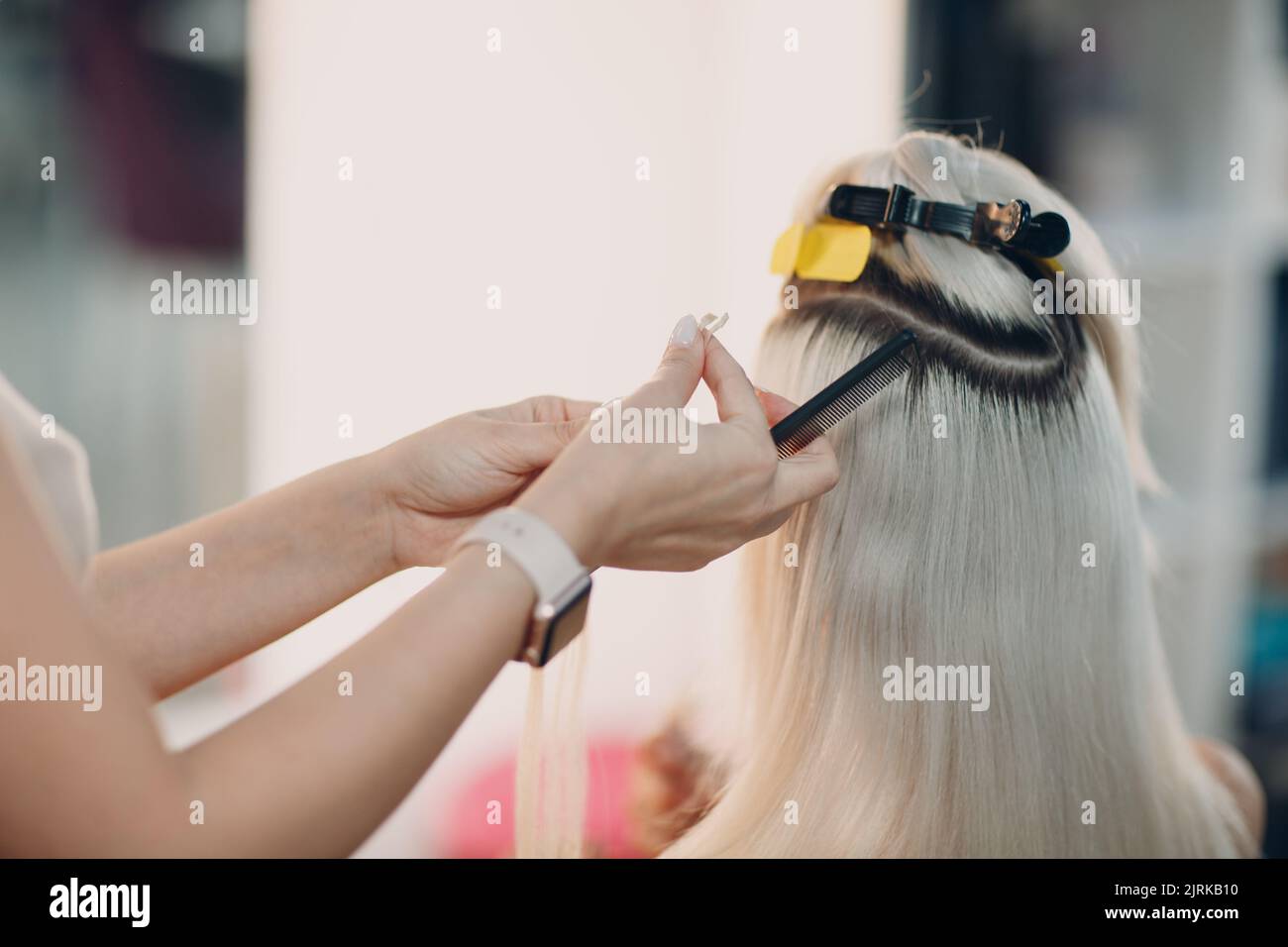 Hairdresser female making hair extensions to young woman with blonde