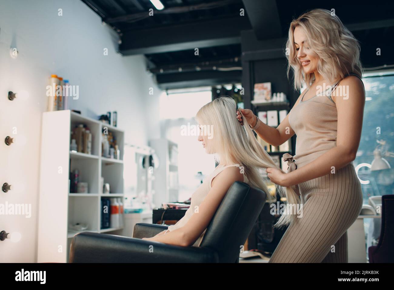 Hairdresser female making hair extensions to young woman with blonde