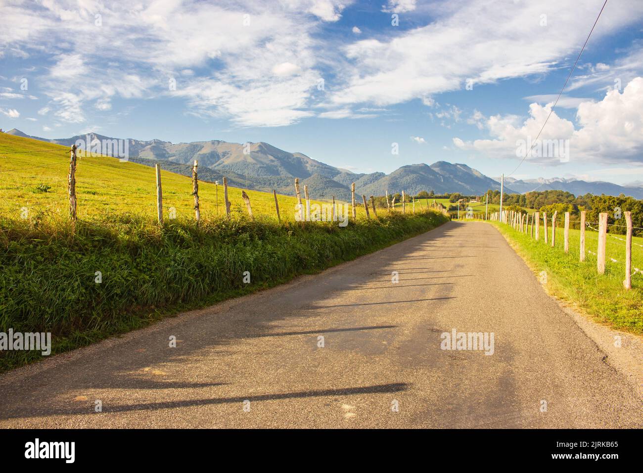 Amazing landscape with mountains on background. Wide empty road in countryside. Camino de Santiago landscape. Fields with mountains on sunny day. Stock Photo