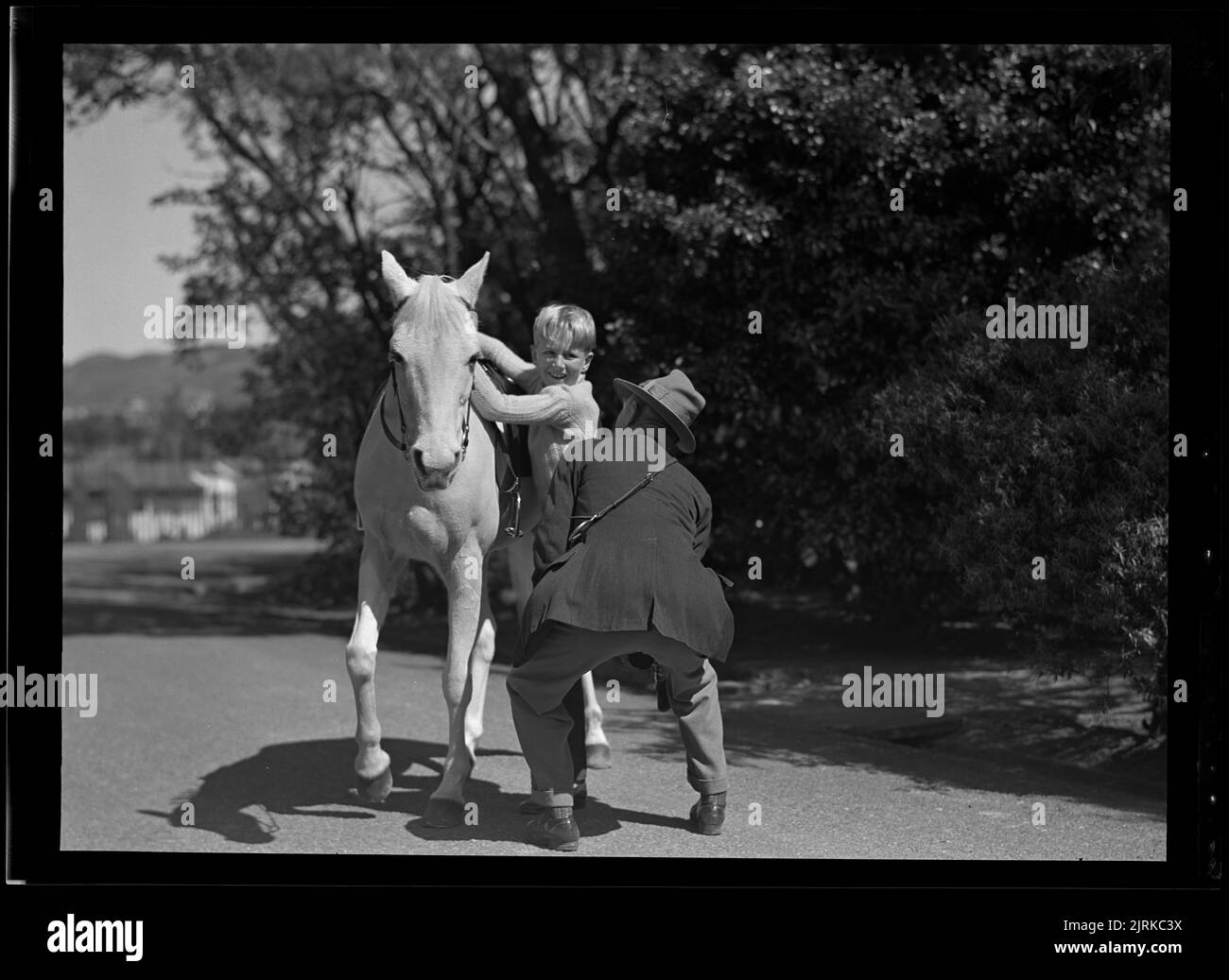 Wanless (Government House groom) helping Simon Galway onto horse in grounds of Government