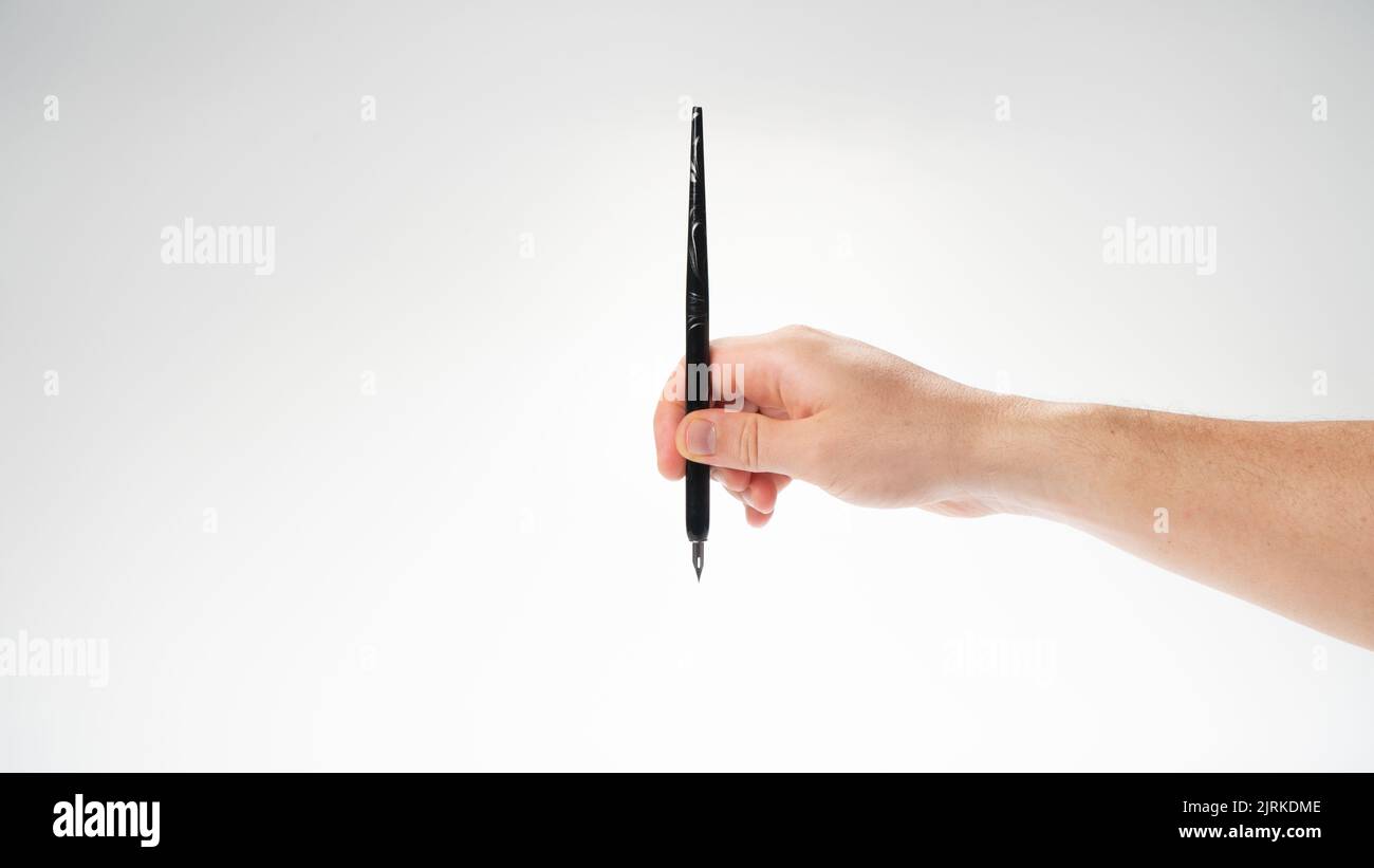 male right hand holds a calligraphy pen on a white background, gesture drops into the inkwell. High quality photo Stock Photo