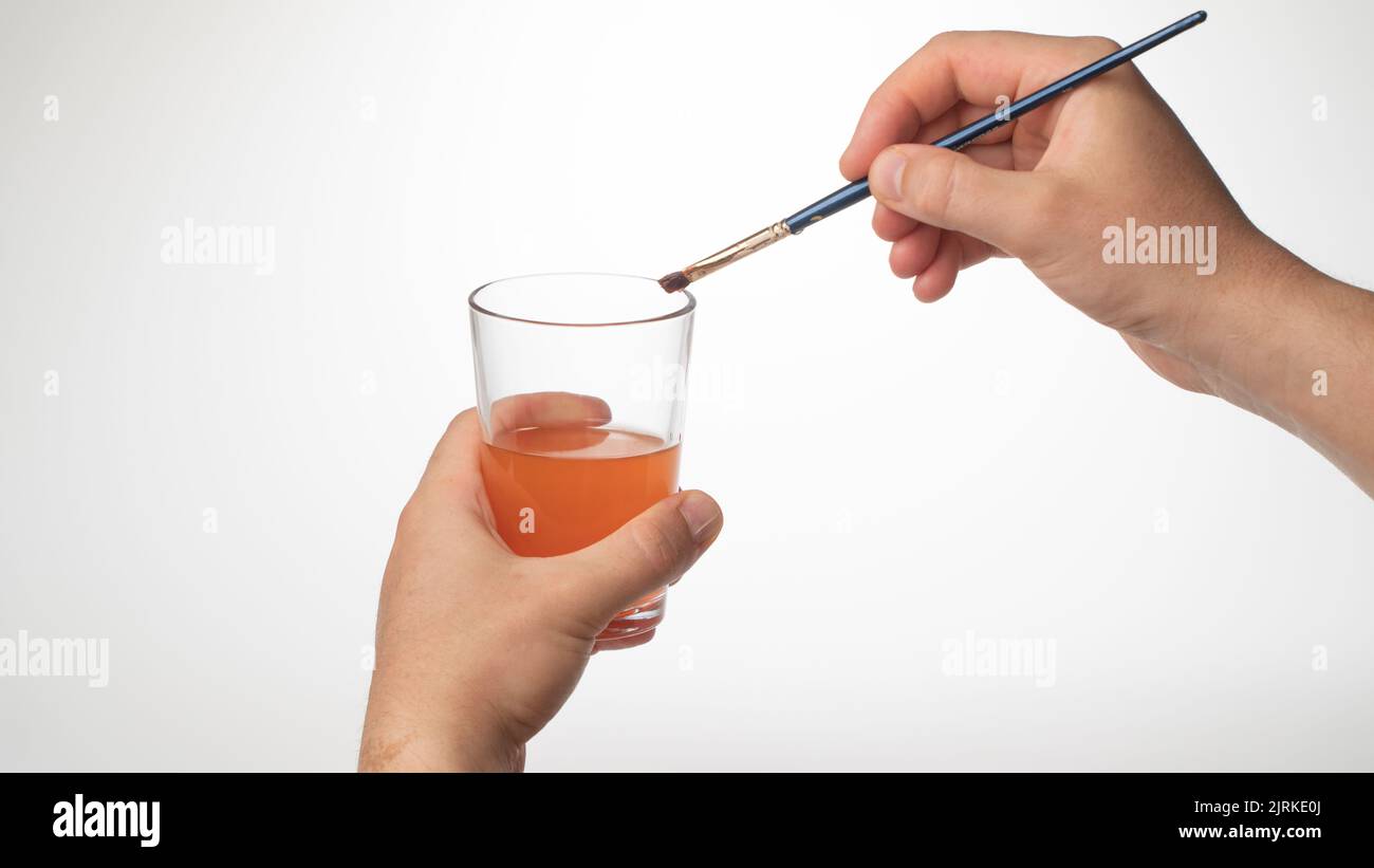 men's hand cleans the brush from the paint in a glass of water Stock Photo