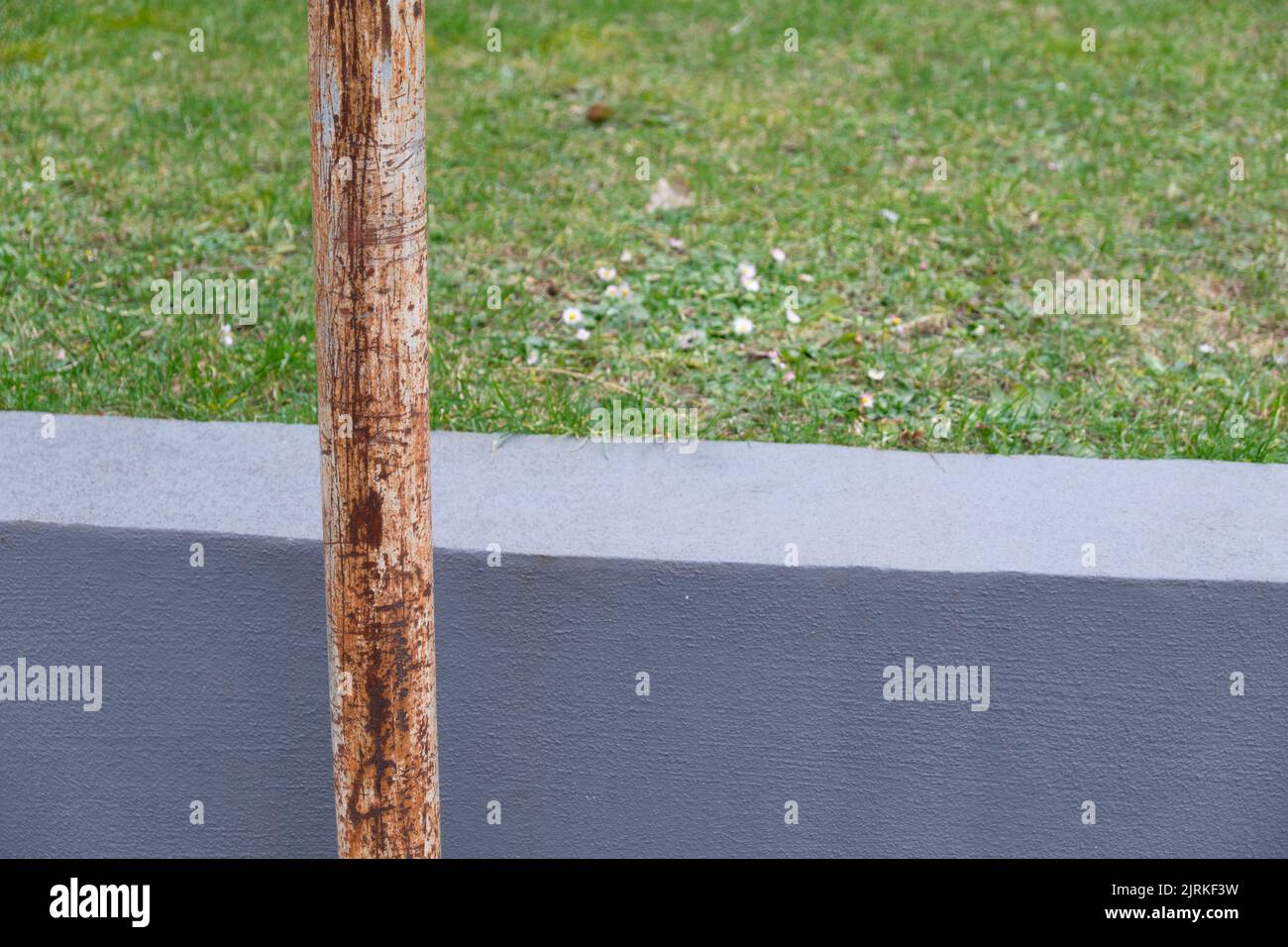 Abstract still life with a rusty old signpost, green grass and a grey concrete wall. Seen in Germany in February. Stock Photo