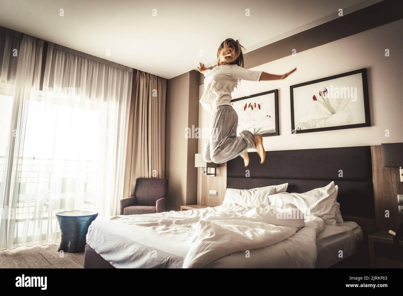 Woman having fun and jumping with bathrobe on bed in hotel room Stock