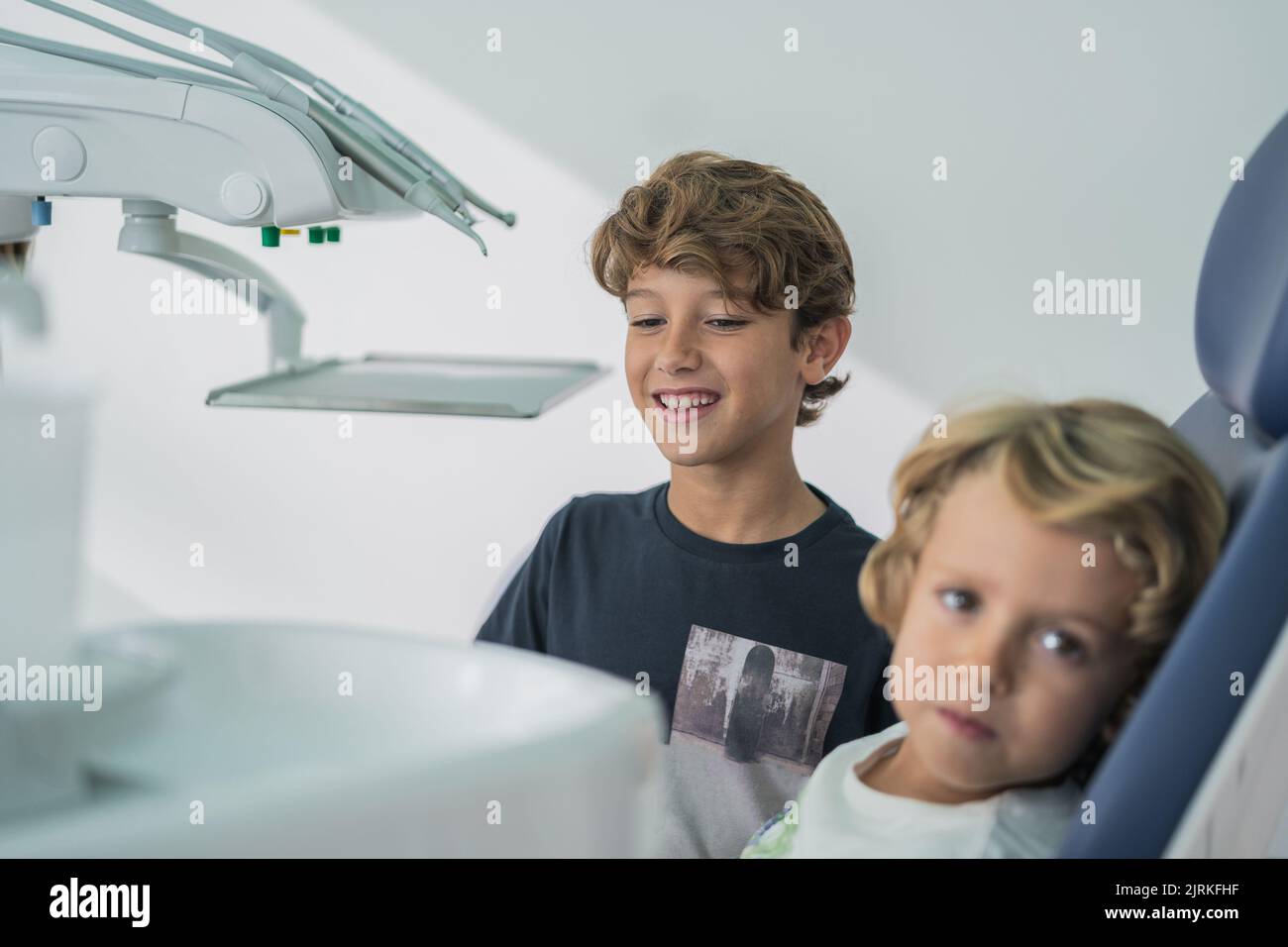 Friendly boy smiling and comforting little brother during visit in modern dental clinic Stock Photo