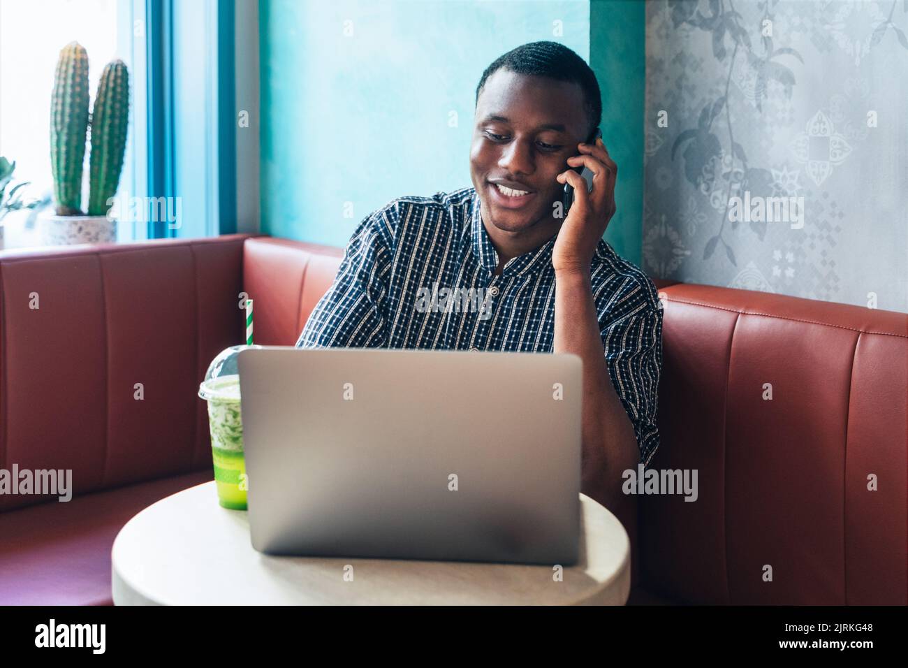 Content African American male entrepreneur speaking on cellphone against table with netbook and smoothie in restaurant Stock Photo