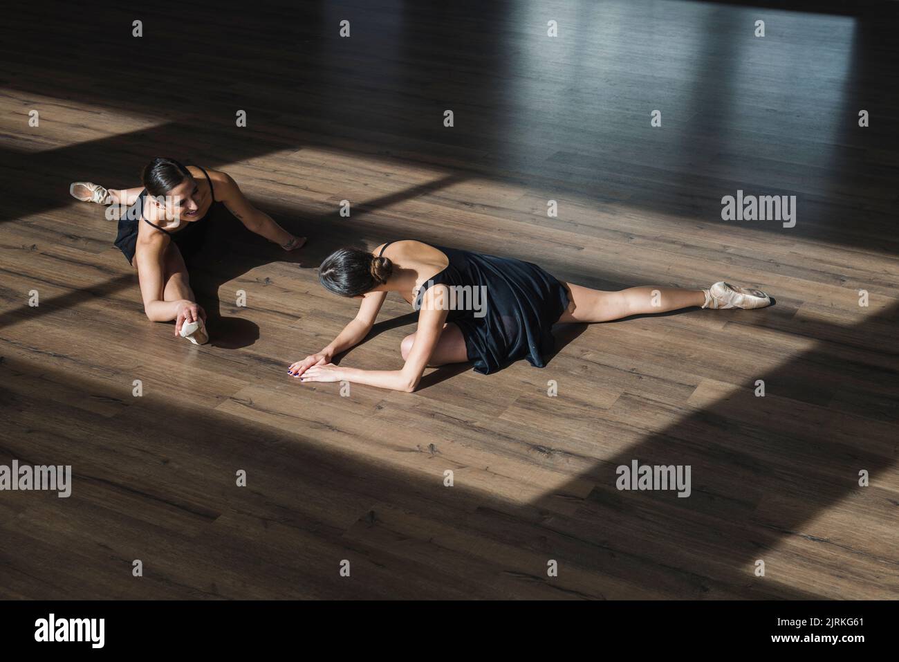 Couple of young woman dancers doing a stretching routine on the floor ...
