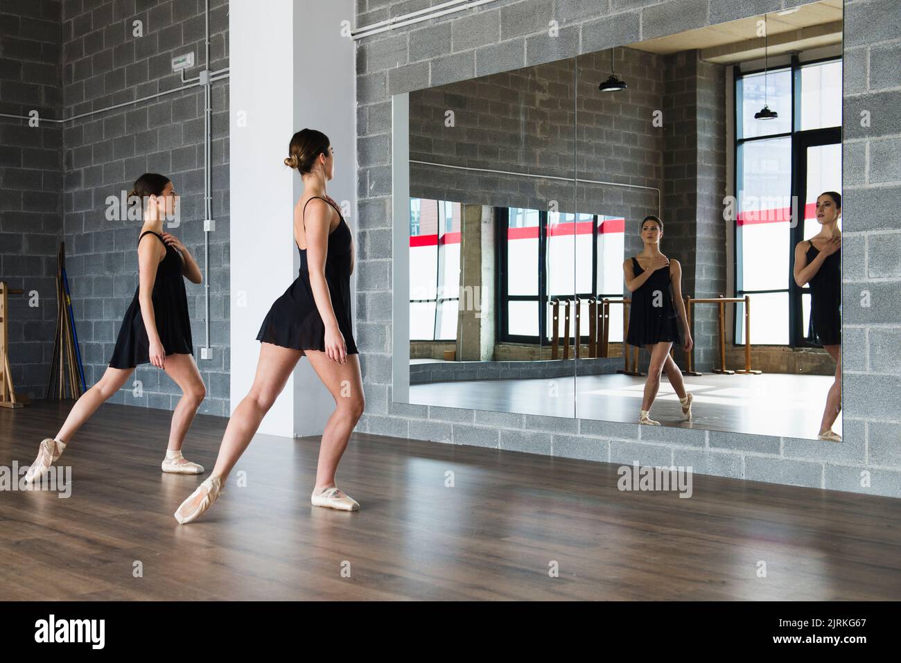 Couple of young woman dancers doing a stretching routine in front of a mirror at dance studio