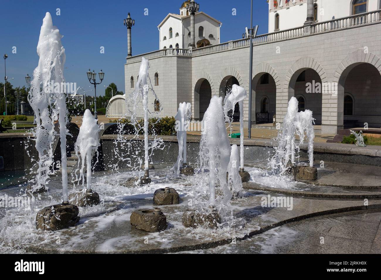 Splashes of water from a fountain against the background of a white church. Natural texture of only fountain water. Effect of high waves in hot summer Stock Photo