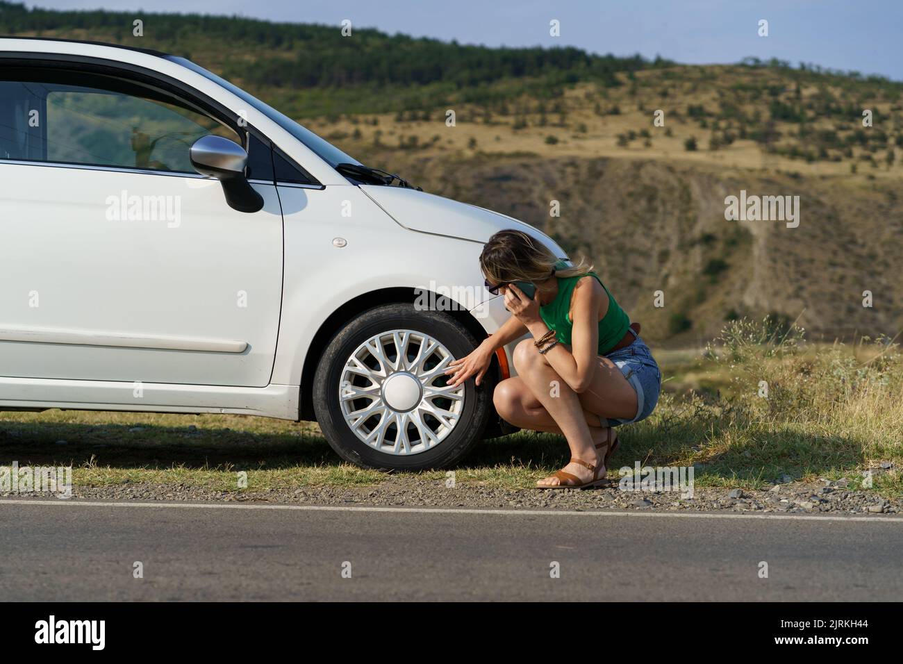 Woman calls to auto mechanic asking for help with changing wheel tire of white car on roadside Stock Photo