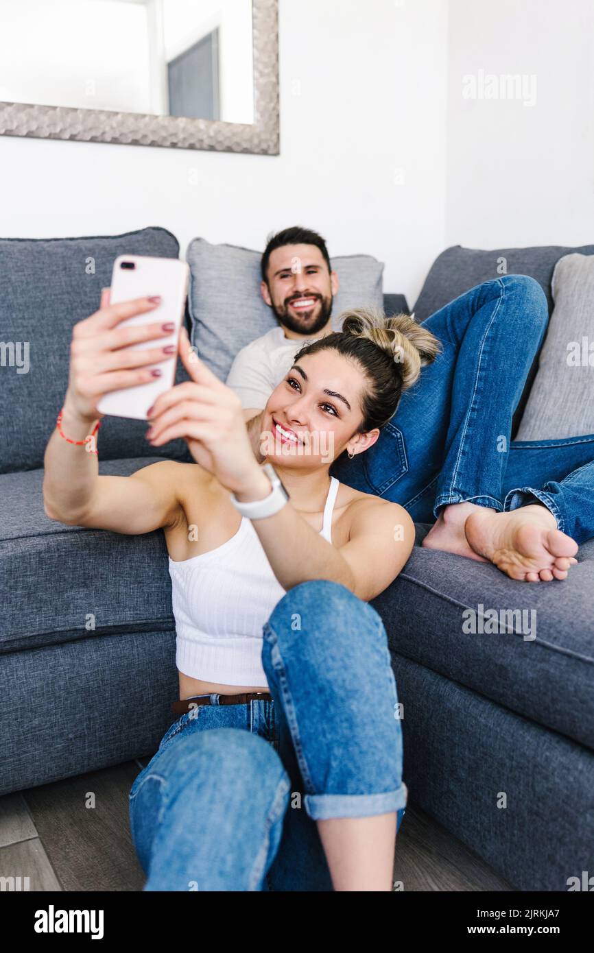 Positive ethnic couple sitting in living room at home and taking self shot on mobile phone Stock Photo