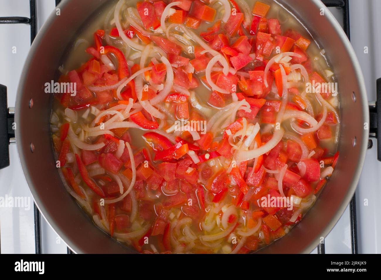 Top view of chopped tomatoes and onions in pot cooking on stove for