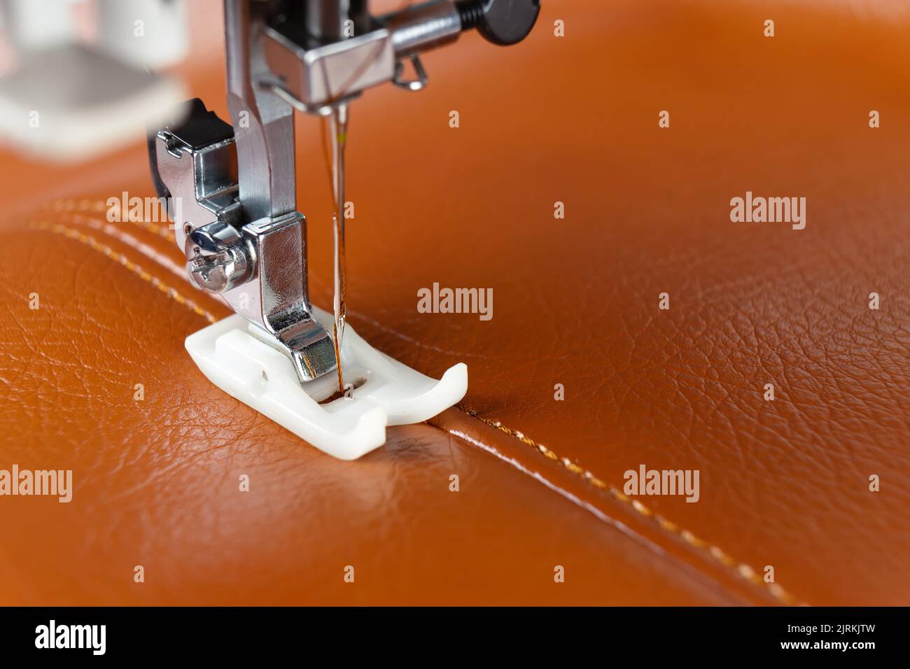 Modern sewing machine presser foot with a needle sews brown leather