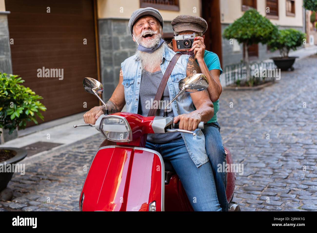 Crop of a modern senior couple with masks riding on a motorcycle and taking pictures while driving through town Stock Photo