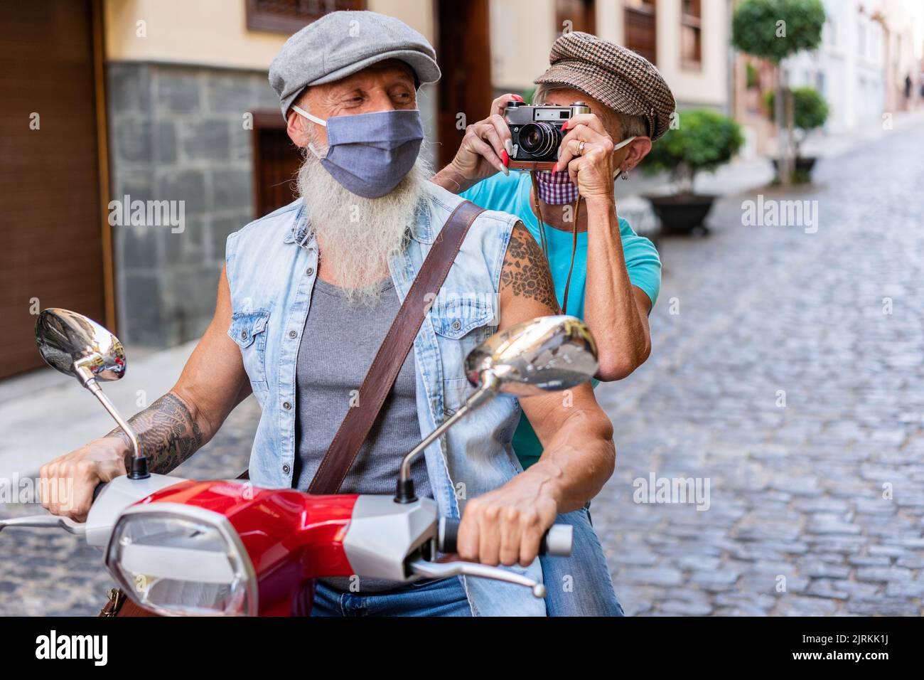 Crop of a modern senior couple with masks riding on a motorcycle and taking pictures while driving through town Stock Photo